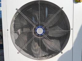A large air conditioning fan is visible on a building's side, providing airflow under a bright, sunny sky in a warm environment photo