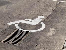 A parking space marked with a disability symbol is positioned directly above a drain in a public lot during bright daylight photo