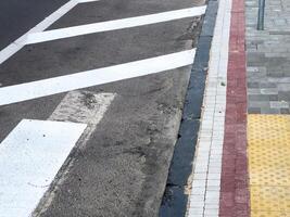 At an urban intersection, white road markings are visible alongside a textured sidewalk with tactile paving, indicating pedestrian areas photo