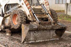 A skid steer loader with a dirt-filled bucket actively works on a muddy construction site, preparing for new building projects photo