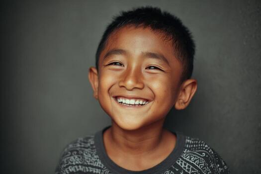 A young boy smiles while standing in front of a gray wall photo