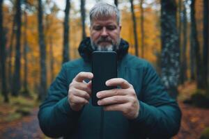 Bearded man capturing autumn colors with smartphone in forest photo