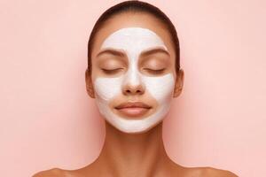 Skincare routine featuring a woman applying a facial mask on smooth skin against a pastel pink background photo