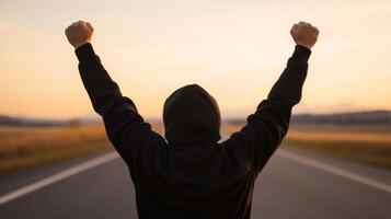 Victory moment of a young person celebrating success outdoors at sunset on an open road photo