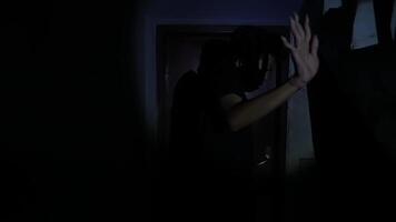 A shadowy figure stands in a dimly lit hallway, raising a hand in a gesture of stop. The scene evokes a sense of suspense and mystery, with dark tones and a focus on the figure's silhouette. video
