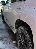 Foam flows down the side of a white large SUV at car washing service photo
