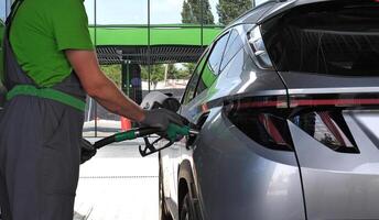 Petrol Station Worker holds a filling nozzle in his hands while refueling a car at a gas station photo
