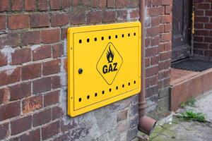 Bright yellow gas meter box displaying GAZ text and flame symbol mounted on an aged brick wall, symbolizing residential energy supply and essential utility infrastructure photo