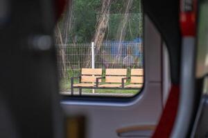 A row of three empty wooden public benches with sturdy black metal frames, observed from a tranquil vehicle window, depicting a calm urban transit waiting area photo