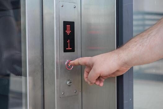Person pressing the down arrow button on an elevator control panel, displaying the first floor and direction for convenient building access photo