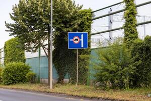 Blue road sign with truck prohibition and left arrow, signifying the end of restriction or an alternative route near a sound barrier photo
