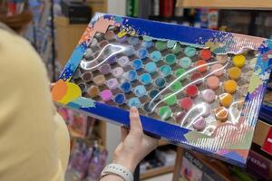 Shopper holds a vibrant paint by number art kit box filled with numerous small colorful paint pots, inspiring creativity and artistic expression for hobbyists photo