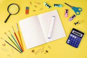 Bright flat lay of colorful school and office supplies, featuring a notebook, pen, and calculator, on a yellow background, promoting learning and creativity photo