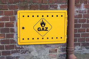 Yellow gas warning box with flame symbol and GAZ text mounted on an old brick wall, representing public utility and energy supply safety infrastructure photo
