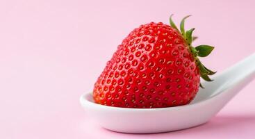 Vibrant red strawberry resting on a white ceramic spoon, soft pink background. photo