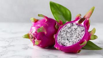 Fresh ripe dragon fruit, one cut open, showing seeds on marble. Healthy exotic food. photo