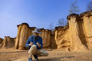 Asian geologist is exploring and surveying the sample rock on the natural sandstone canyon quarry resource site for scientific research and archeology for understanding mother earth photo