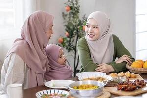 Middle eastern muslim lady in hijab is talking to her mother in law and baby daughter while waiting for dinner during Eid Mubarak, Ramadan festival for culture and religion photo