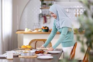 Middle eastern muslim lady in hijab is preparing food and dinner table arrangement for family feast at night during Eid Mubarak, Ramadan season with naan bread, biryani for culture and religion photo