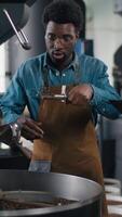 Multinational men factory baristas inspect hot roasted coffee inside spinning machine espresso Caucasian expert clipboard African workers preparation process industrial automation equipment quality video