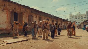 A dynamic dance group performing in an urban setting with rustic buildings and string lights overhead. The dancers showcase a variety of styles and outfits, creating an energetic atmosphere. video