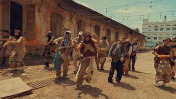 A dynamic group dance performance in an urban setting, featuring multiple dancers in coordinated movements. The background shows old buildings and a lively atmosphere. video