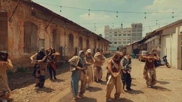 A group of people dressed in tattered clothing performing a synchronized dance or movement in an outdoor setting with old buildings and string lights in the background. video