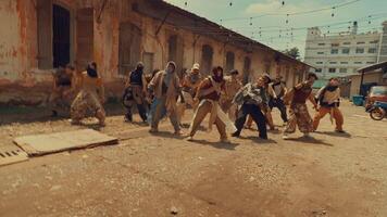 A group of dancers performing dynamic movements in a rustic outdoor setting, with an industrial backdrop. The scene captures energy and motion, showcasing diverse clothing styles. video