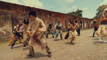 A group of dancers performing a choreographed routine outdoors, showcasing dynamic movements and expressive gestures. The setting features an industrial backdrop with a rustic building and blue sky. video