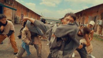 A dynamic dance performance in an industrial setting, featuring a group of dancers in coordinated movements. The backdrop includes weathered buildings and a cloudy sky video