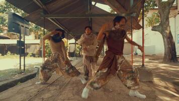 A person performing a dynamic dance move in an outdoor setting with rustic architecture. The scene captures movement and energy, surrounded by greenery and old structures. video