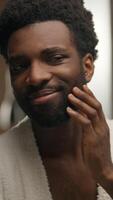 African American man looking at mirror reflection hotel bathroom smiling bearded guy shaving beard lotion gel cream soft skin shave face grooming morning hygiene male cosmetics facial care moisturize video