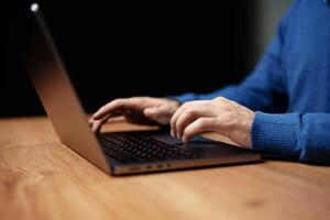 Hands typing on laptop at wooden desk in a cozy setting during evening hours with soft lighting photo