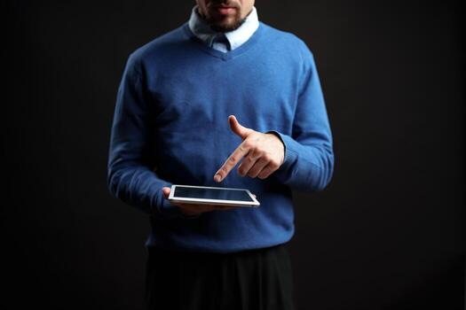 Man in blue sweater using tablet while standing against a dark background in a modern setting photo