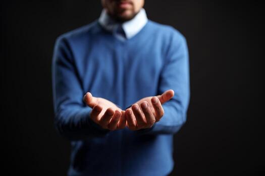 Man extending hands in a welcoming gesture against a dark background during a studio session photo