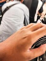 Close-up shot of a brown-skinned hand with an unknown person's back in the background. A crowd of people jostling and pressing against each other. Negative space photo