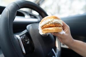 Asian lady holding hamburger to eat in car photo