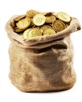 A burlap sack filled with gold coins spilling out on a white background in a studio shot photo