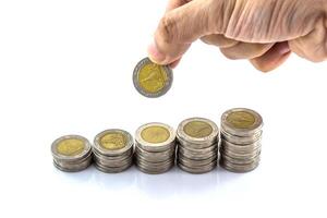 Hand holding a coin and stacking coins on a white background photo