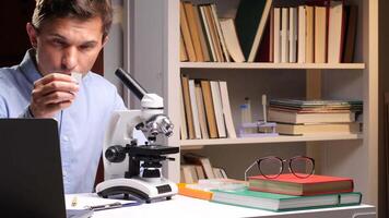 Close-up portrait scientist examining a sample slide under a microscope in a lab, surrounded by research materials and using a laptop for documentation and analysis video