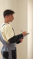 A man in overalls is writing on a clipboard video
