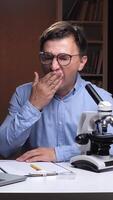 vertical student, scientist at desk with microscope tired and yawning. Tired man yawning video