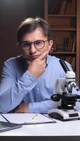 vertical Scientist thinking at desk with microscope, laptop and books in laboratory or office video