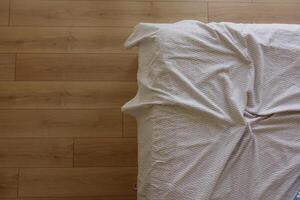Messy bed with wrinkled sheets on wooden floor photo