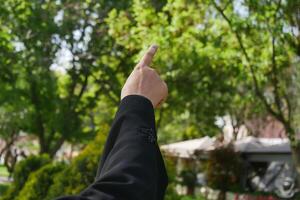 Hand pointing towards lush green trees in a garden photo