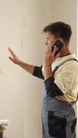 A man in overalls talking on a cell phone video