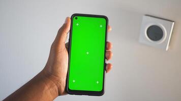 Hand holding smartphone with green screen and wall elements photo