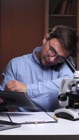 A man in glasses is using a tablet computer and a microscope video