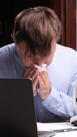 A man blowing his nose while using a laptop video