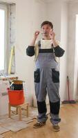 Vertical exhausted painter rubbing his tired eyes while holding his glasses, taking a break during apartment renovation, surrounded by painting tools and equipment video
